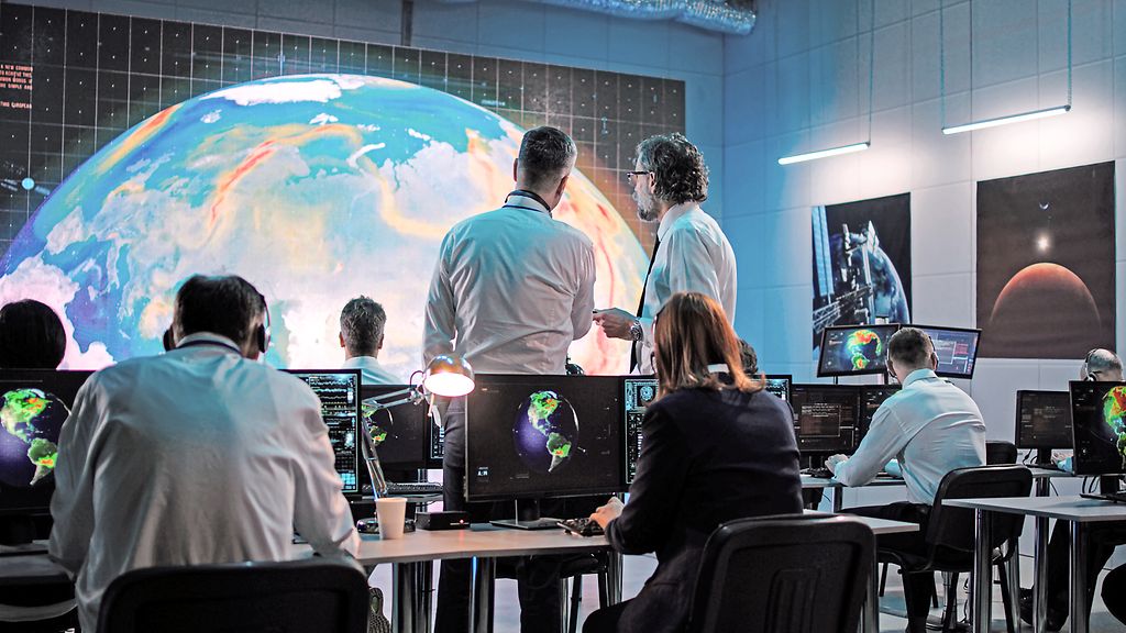 Men discussing hot air movements on Earth while team of employees using computers during work on global warming problem